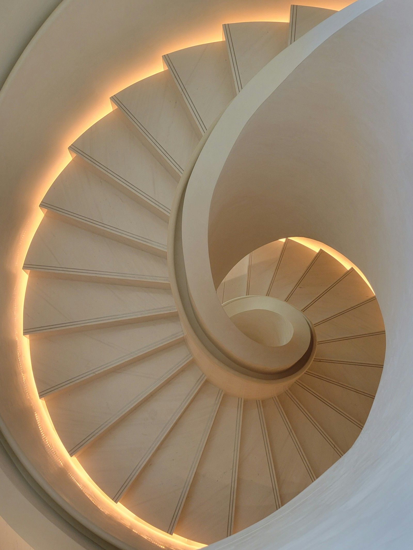 Spiral stone staircase seen from below, its edge lit by a warm hidden light